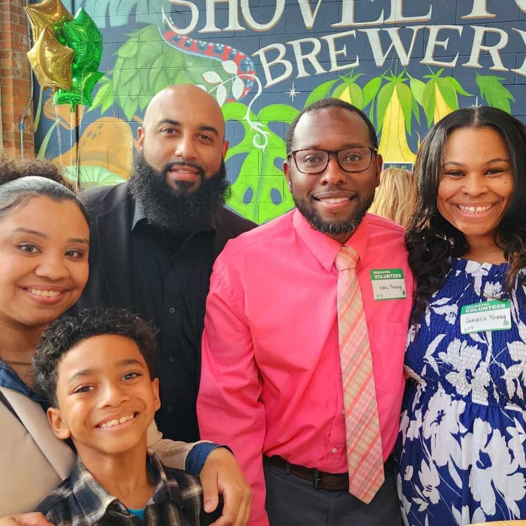 Four adults and a child smile in front of a Shoveltown Brewery sign